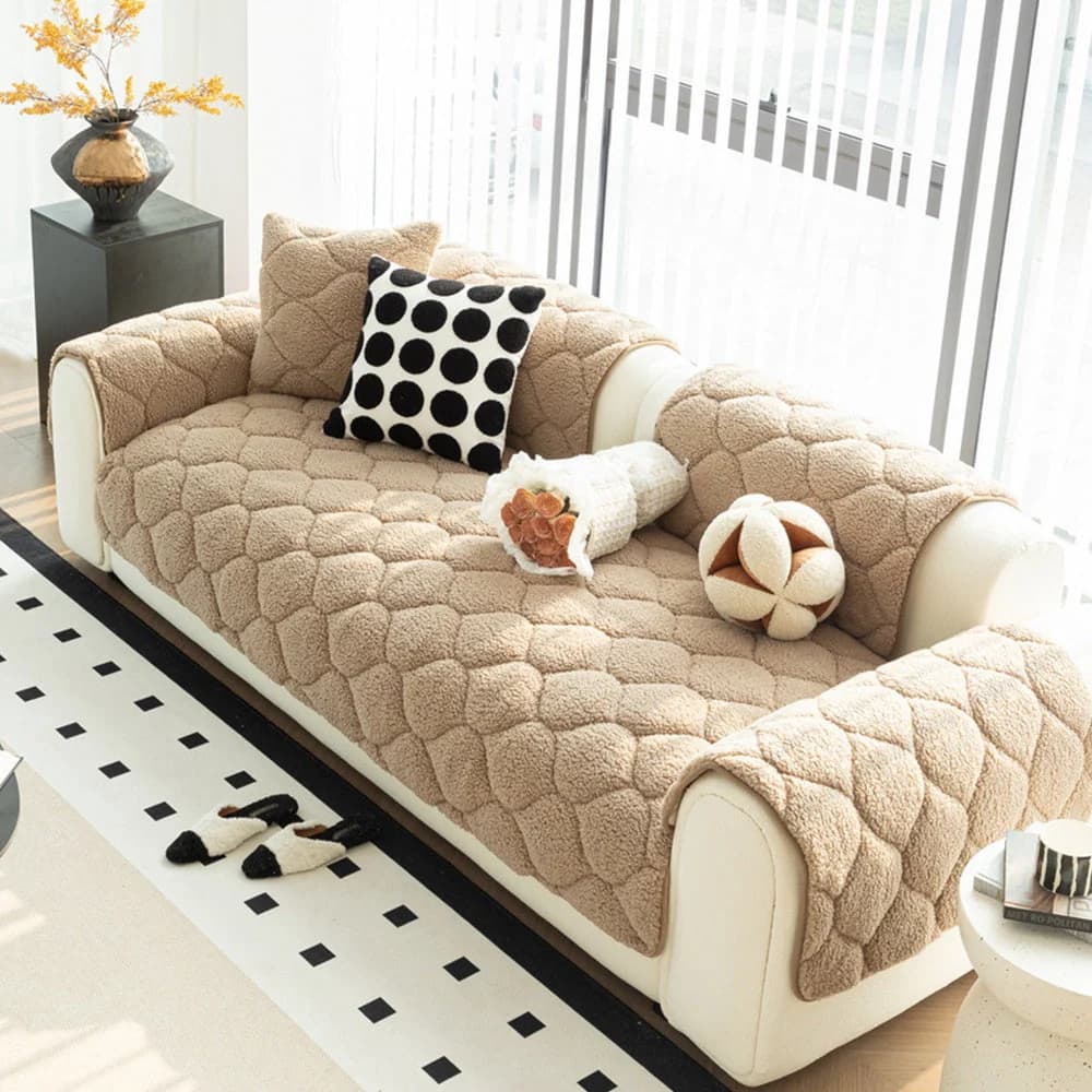 Small dog sleeping comfortably on a beige quilted sherpa fleece sofa cover in a bright modern living room