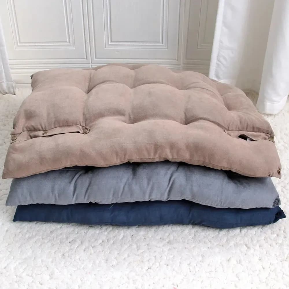 Beige and grey plush tufted pet bed cushions stacked together on a wooden floor in a bright room.
