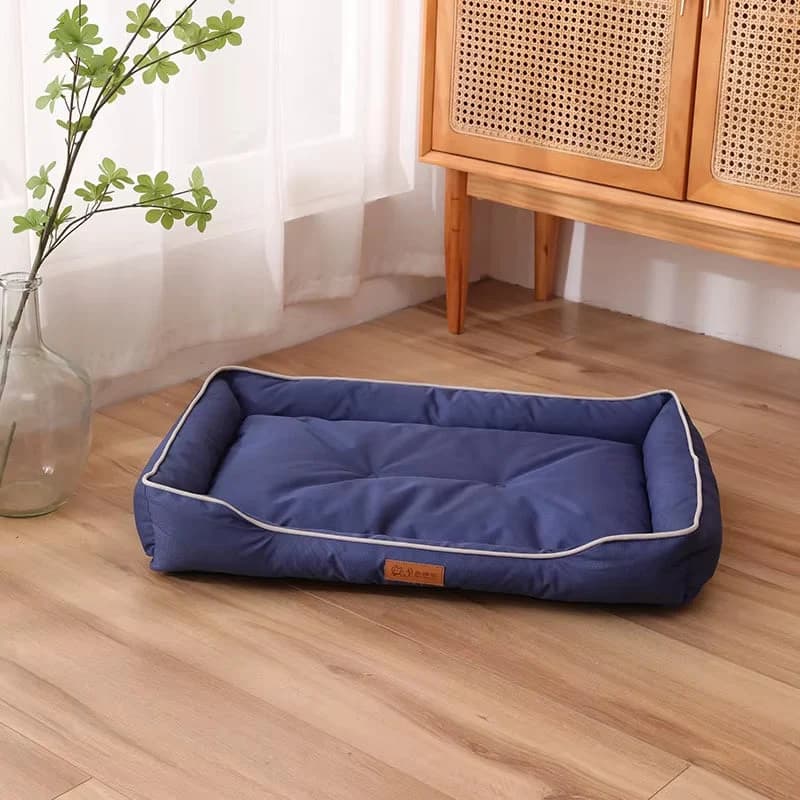 Blue rectangular cushioned dog bed with raised supportive sides displayed in a bright home.
