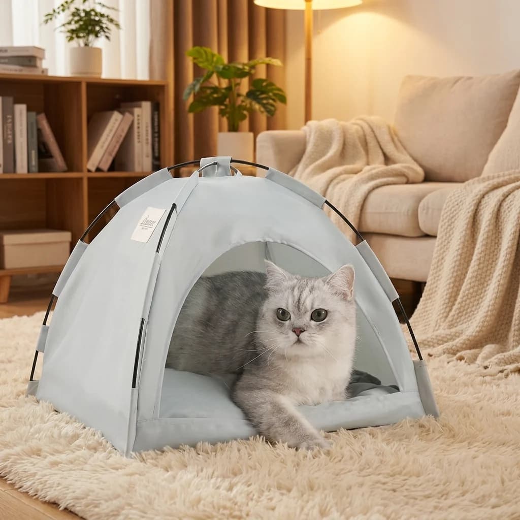 Grey cat resting inside a cosy light grey portable tent bed beside a sofa in a warm home interior