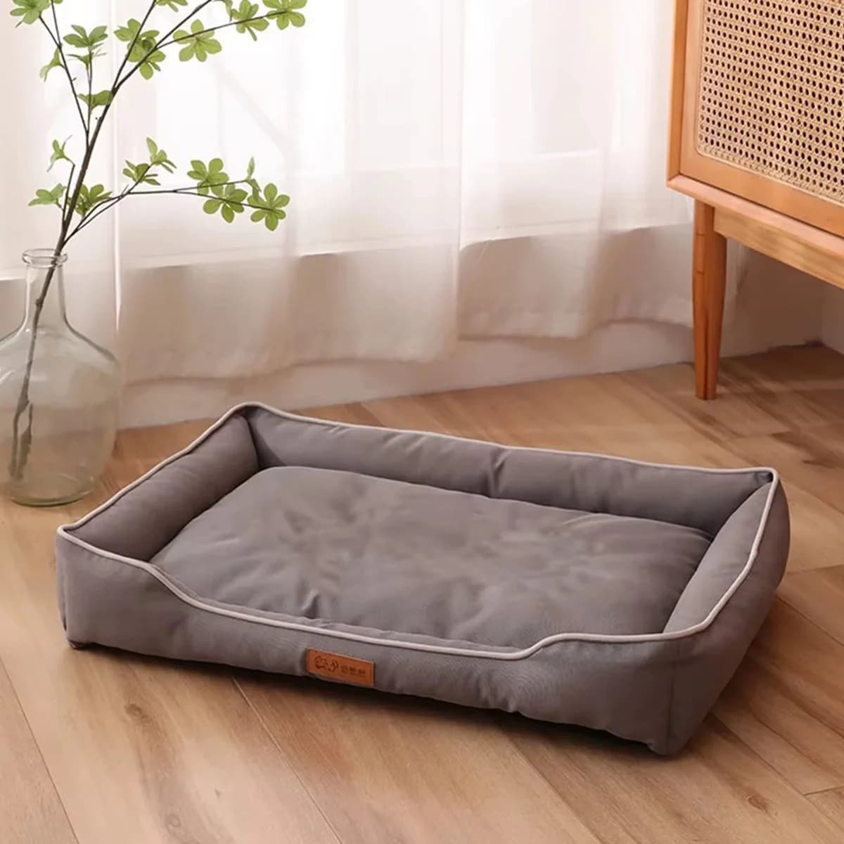Grey rectangular cushioned dog bed with raised supportive sides displayed on a wooden floor.
