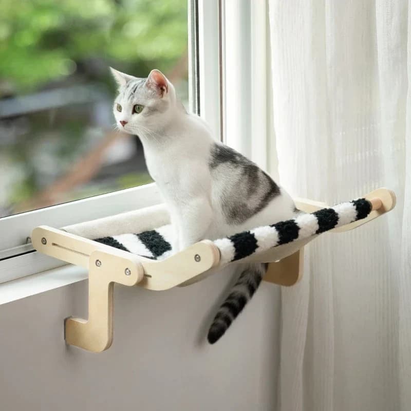 White and grey cat relaxing on a raised wooden window perch beside a bright window.